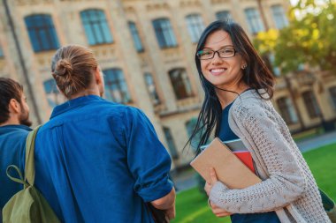 Sırt çantaları ve kitaplarıyla kampüsün önündeki öğrencilerin arka görünüşü
