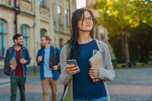 キャンパスに立っている間に携帯電話を使用してバックパックを持つ若い女性学生離れて見て — ストック写真