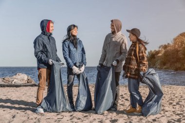Sahili temizledikten sonra konuşan ve gülümseyen gönüllüler ön planda.