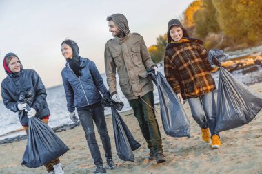 Bir grup arkadaş dışarıda plastik topladıktan sonra yürür ve konuşur.