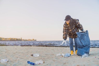 Çöpleri toplayan ve plastikleri çöp torbasıyla temizleyen genç kız.