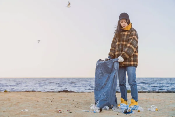 소녀는 모래가 해변의 쓰레기통에 플라스틱 쓰레기를 모은다 — 스톡 사진