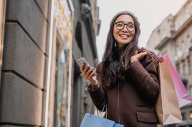 Akıllı telefon kullanan Asyalı kadın alışverişin keyfini çıkarırken gözlerini kaçırıyor.