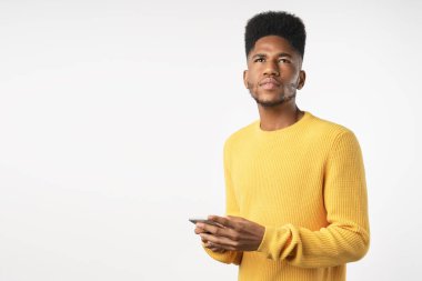 Sıradan bir cep telefonuyla beyaz arka planda duran dalgın Afrikalı genç adamın portresi.