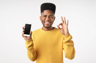 Boş akıllı telefon ekranı gösteren mutlu adam tamam işareti gösterirken ve beyaz arkaplandan kameraya bakarken