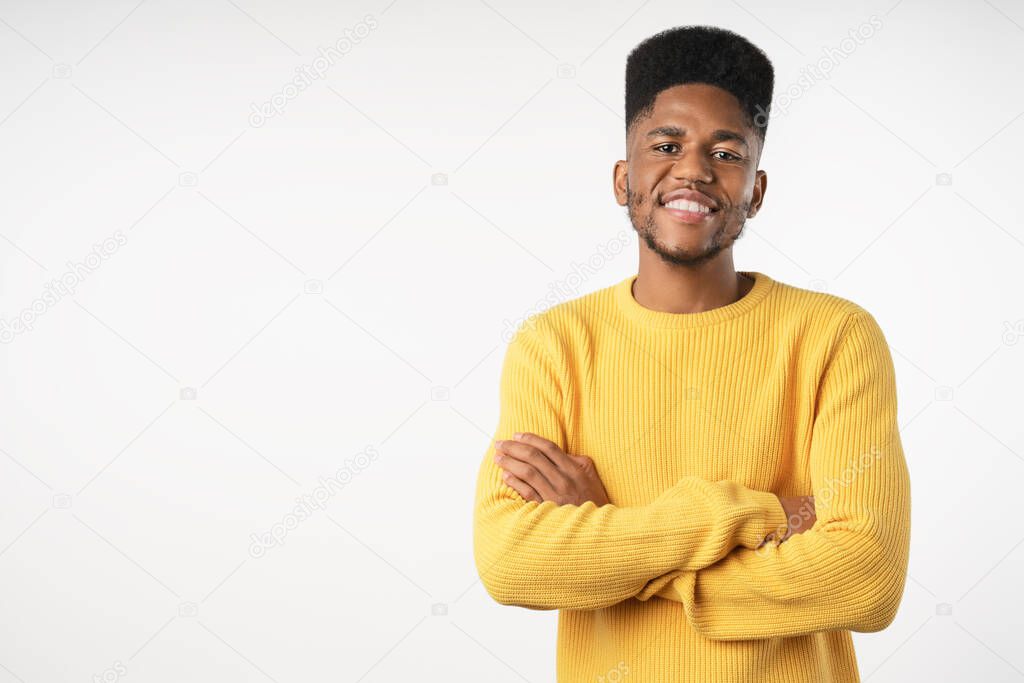 Young handsome man in casual keeping arms crossed and smiling while standing against white background