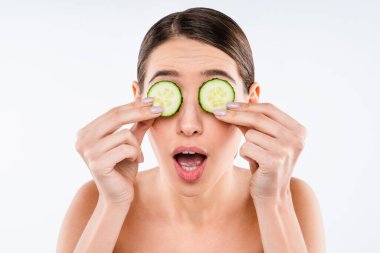 Beyaz arka plan stüdyosunda salatalıkla cilt bakımı yapan güzel genç kadın görüntüsünü kapat.