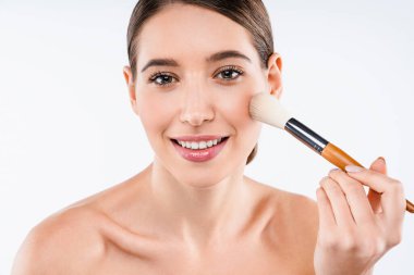 Beyaz arka planda izole edilmiş makyaj fırçasıyla makyaj yapan yarı çıplak, beyaz esmer bir kadının güzel portresi.