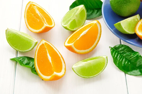 Citrus fruits with green leaves. Orange, lime segments on white wooden surface — Stock Photo, Image