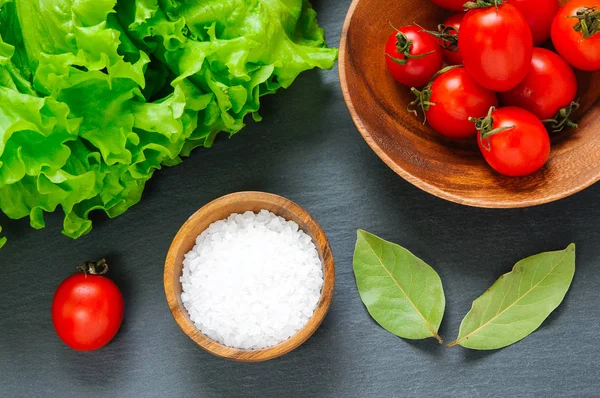 Ansicht von oben: frische Kirschtomaten, Salz und Lorbeerblätter auf schwarzem Hintergrund mit Gewürzen — Stockfoto