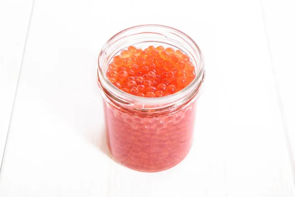 Caviar vermelho em frasco de vidro no fundo de madeira branco — Fotografia de Stock