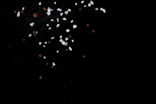 Schwebende Salzkristalle und schwarzer Pfeffer würzen auf schwarz. Kopierraum lizenzfreie Stockfotos