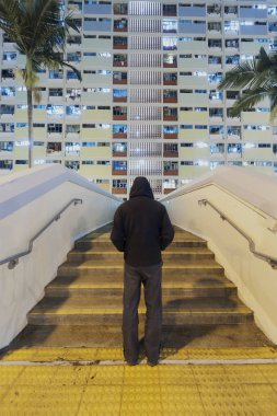 Mysterious man standing in front of high rise residential buidling in public estate in Hong Kong city at night clipart