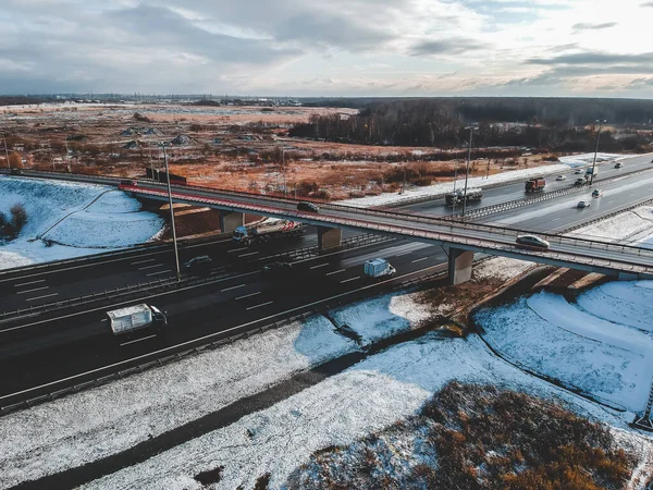 Vista aérea de carretera y puente, tráfico por carretera, bosques y campos cubiertos de nieve, invierno. Rusia, San Petersburgo . — Foto de Stock