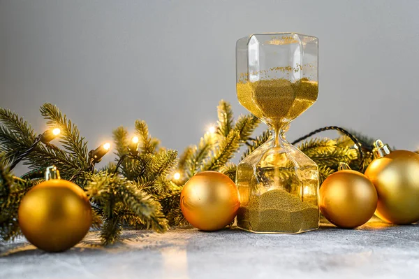 Vánoční pozadí, přesýpací hodiny se zlatým pískem, jedlové větve a vánoční hračky. Koncept blížící se dovolené. Šťastný nový rok. — Stock fotografie