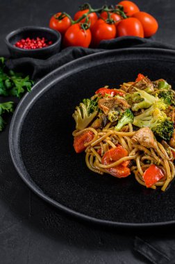 Kızarmış erişte, geleneksel Çin tavası. Yemek çubukları, malzemeler. Sebzeli Asya eriştesi, et. Siyah siyah arka plan. Üst görünüm.