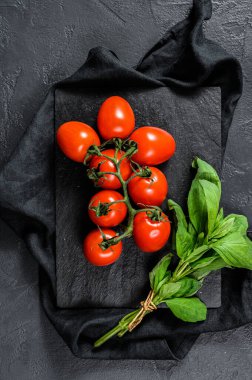 Siyah arka planda fesleğenli kiraz domatesleri. Üst görünüm.