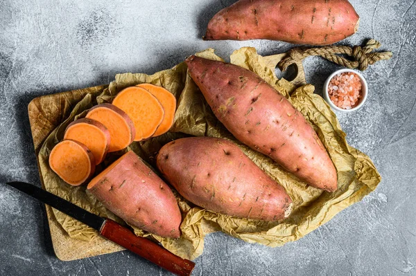 Rohe Süßkartoffeln auf einem Schneidebrett, Bio-Batatas. Gemüse vom Bauernhof. grauer Hintergrund — Stockfoto