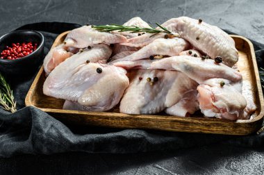Ahşap bir kasede çiğ tavuk kanadı, biberiye ve pembe biber malzemeleri. Çiftlik organik eti. Üst Manzara. Siyah arkaplan