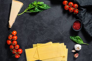 Lazanya pişirme konsepti. Malzemeler, lazanya, fesleğen, vişneli domates, parmesan, sarımsak, biber. Siyah arka plan. Üst Manzara. Metin için boşluk
