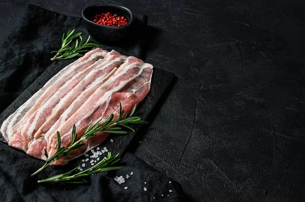 Rauwe bacon op een stenen snijplank. Varkensvlees. Zwarte achtergrond. Bovenaanzicht. Ruimte voor tekst — Stockfoto