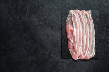 Taş doğrama tahtasında çiğ domuz pastırması. Domuz eti. Siyah arka plan. Üst Manzara. Metin için boşluk