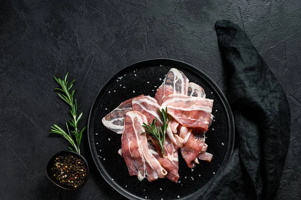 Bacon på svart tallrik, peppar och rosmarin. Ekologiskt kött från jordbruket. Svart bakgrund. Ovanifrån — Stockfoto