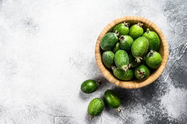 Gri bir arka planda, ahşap bir tabakta yeşil feijoa meyveleri. Tropik meyve feijoa. Üst Manzara. Metin için boşluk