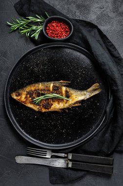 Beyaz bir tabakta pişmiş sazan balığı. Nehir organik balığı. Siyah arka plan. Üst görünüm