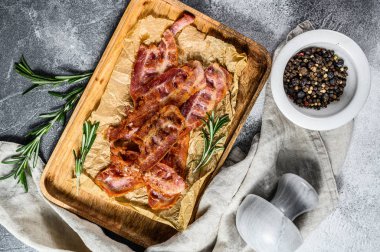 Ahşap doğrama tahtasında kızarmış pastırma. Biberiye ve karabiberle servis et. Gri arka plan. Üst görünüm