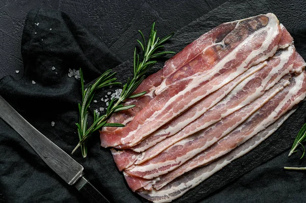 Spek op een stenen snijplank. Varkensvlees. Zwarte achtergrond. Bovenaanzicht — Stockfoto