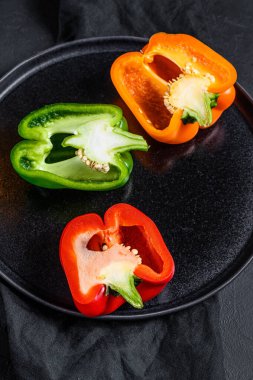 Üç dilim turuncu, yeşil ve kırmızı dolma biber. Siyah arka plan. Üst görünüm