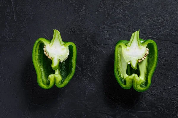 Cut green sweet pepper, two halves. Black background. Top view. Space for text.