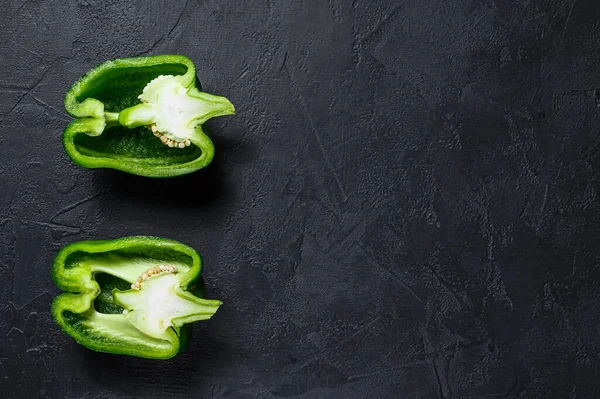 Cut green sweet pepper, two halves. Black background. Top view.