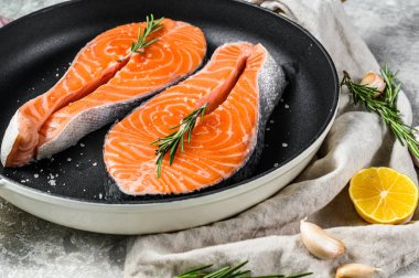 Kızartma tavasında çiğ somon bifteği. Sağlıklı deniz ürünleri. Gri arka plan. Üst görünüm