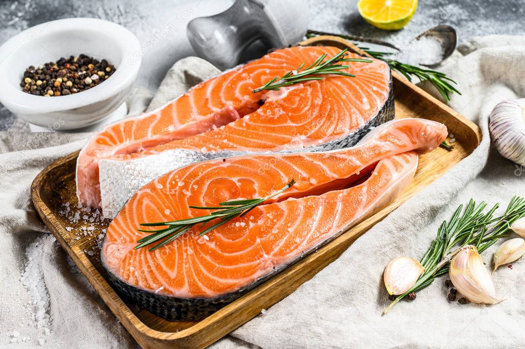 Raw salmon steak on a wooden tray with spices. Healthy seafood. Gray background. Top view