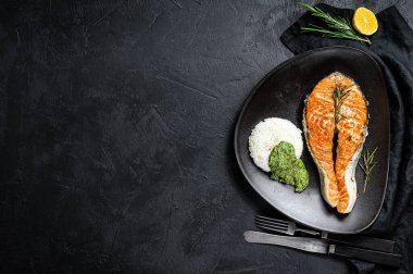 Pirinç ve ıspanakla süslenmiş ızgara somon bifteği. Siyah arka plan. Üst Manzara. Metin için boşluk