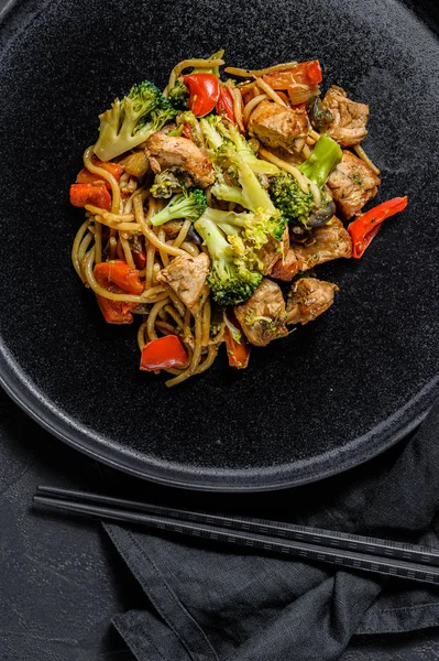Mélanger les nouilles frites, wok chinois traditionnel. baguettes, ingrédients. Nouilles asiatiques aux légumes, viande. Fond noir foncé. Vue du dessus . — Photo