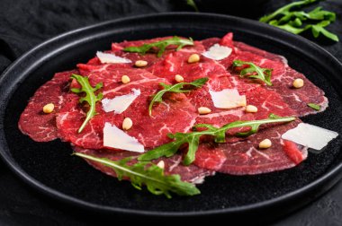 Siyah tabakta sığır eti, parmesan sosu, peynir ve roka. Siyah arka plan. Üst görünüm