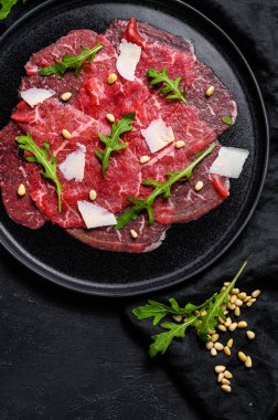 Siyah tabakta sığır eti, parmesan sosu, peynir ve roka. Siyah arka plan. Üst görünüm