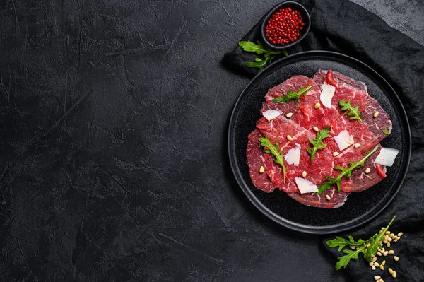 Marbled beef carpaccio with arugula and parmesan cheese. Black background. Top view. Space for text — Stock Photo, Image