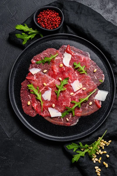 Gemarmerde rundercarpaccio met arugula en parmezaanse kaas. Zwarte achtergrond. Bovenaanzicht — Stockfoto