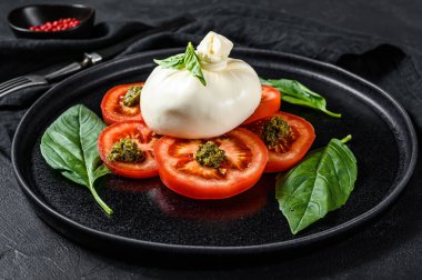 Bufalo burrata peyniri taze domates ve fesleğen yapraklarıyla servis edilir. Siyah arka plan. Üst görünüm