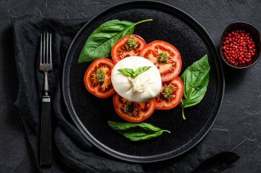 Bufalo burrata peyniri taze domates ve fesleğen yapraklarıyla servis edilir. Siyah arka plan. Üst görünüm