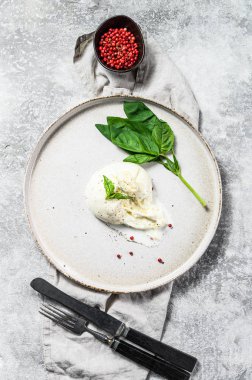 Basil yapraklı beyaz tabakta Burrata peyniri. Gri arka plan. Üst görünüm