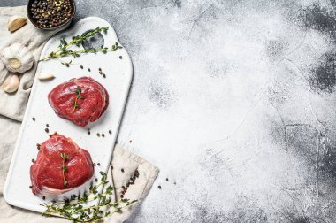 Beyaz kesim tahtasında çiğ fileminyon biftek. Sığır filetosu. Gri arka plan. Üst Manzara. Metin için boşluk