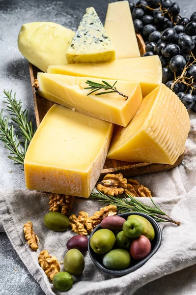 Diferentes pedaços de queijo com azeitonas e uvas. Deliciosos lanches variados. Fundo cinzento. Vista superior — Fotografia de Stock