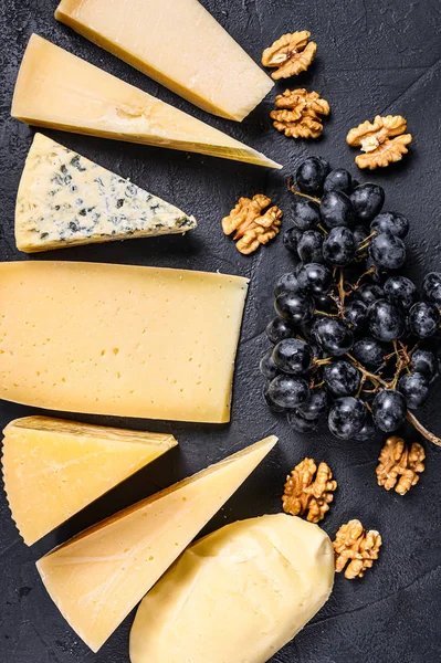 Diferentes tipos de deliciosos queijos com nozes e uvas. Fundo preto. Vista superior — Fotografia de Stock