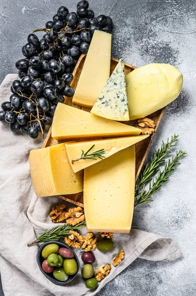Diferentes pedaços de queijo com azeitonas e uvas. Deliciosos lanches variados. Fundo cinzento. Vista superior — Fotografia de Stock