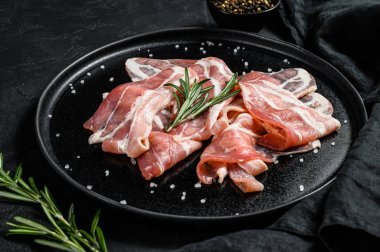 Siyah tabakta çiğ domuz pastırması, biber ve biberiye. Çiftlik organik eti. Siyah arka plan. Üst görünüm